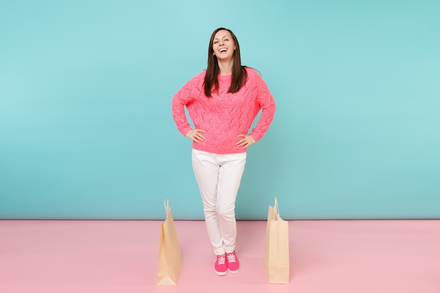 Retrato de mulher em calça branca de malha rosa suéter segurando sacolas multicoloridas com compras