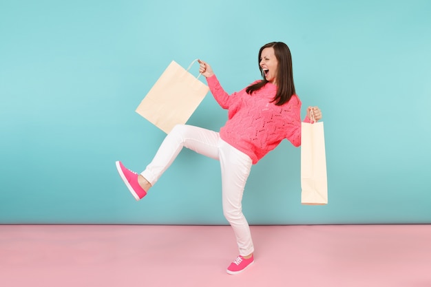 Retrato de mulher em calça branca de malha rosa suéter segurando sacolas multicoloridas com compras