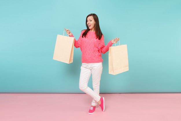 Retrato de mulher em calça branca de malha rosa suéter segurando sacolas multicoloridas com compras