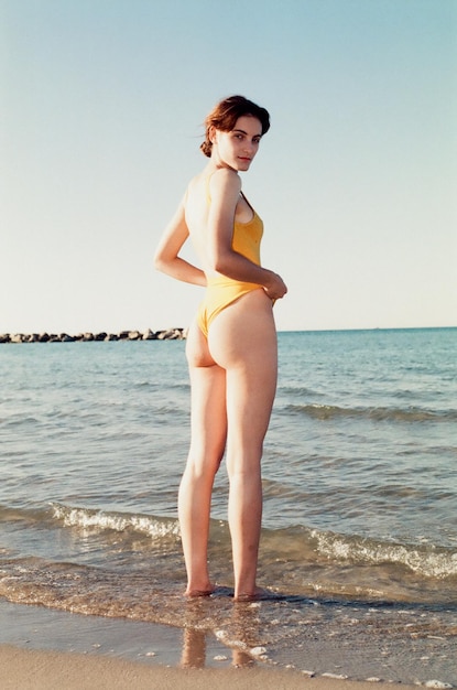 Foto retrato de mulher em fato de banho de pé na praia contra o céu claro