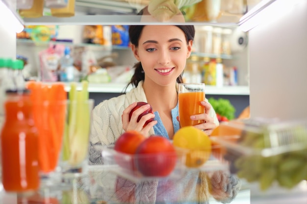 Retrato de mulher em pé perto de geladeira aberta cheia de frutas e legumes saudáveis Retrato de mulher