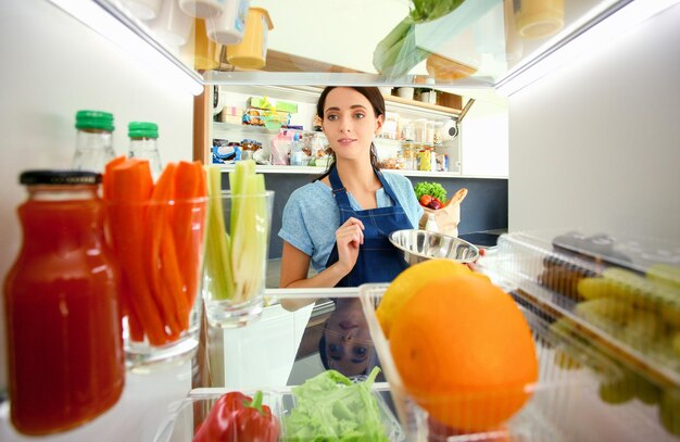 Retrato de mulher em pé perto de geladeira aberta cheia de frutas e legumes saudáveis Retrato de mulher