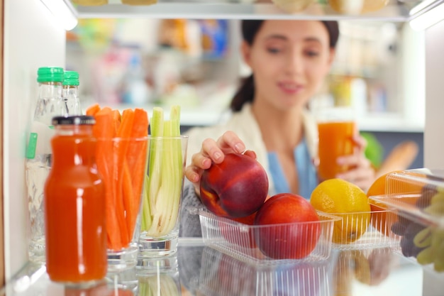 Retrato de mulher em pé perto de geladeira aberta cheia de frutas e legumes saudáveis Retrato de mulher