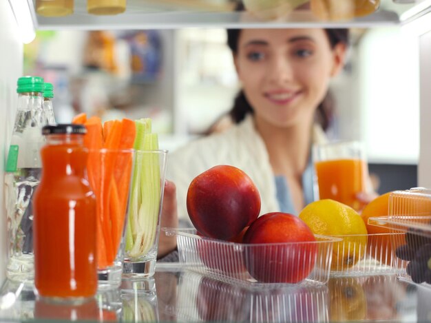 Retrato de mulher em pé perto de geladeira aberta cheia de frutas e vegetais saudáveis