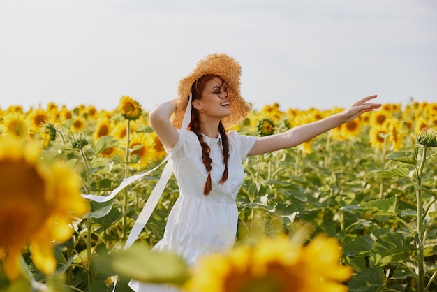 Retrato de mulher em um chapéu de palha em um vestido branco um campo de campos agrícolas de girassóis