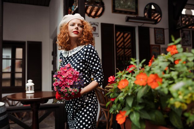 Retrato de mulher em uma boina e vestido azul segurando um buquê de flores ao fundo do restaurante