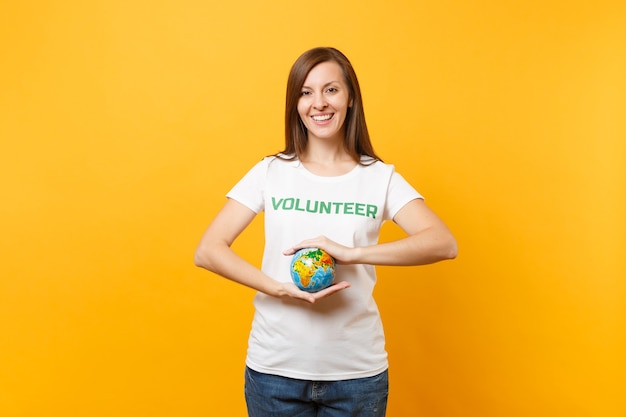 Retrato de mulher em uma camiseta branca com voluntário de título verde de inscrição escrita segurar nas palmas das mãos Globo do mundo terra isolado em fundo amarelo. Ajuda de assistência gratuita voluntária, conceito de graça de caridade.