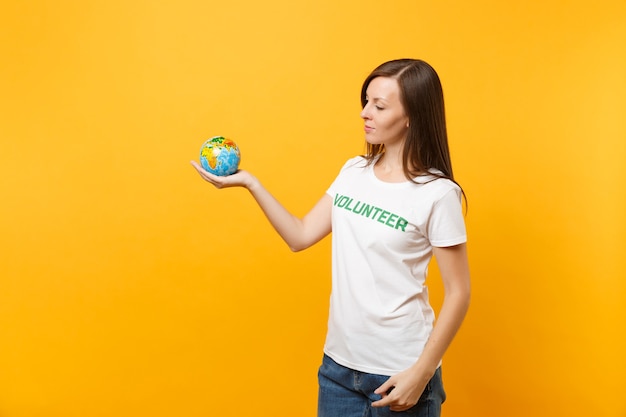 Foto retrato de mulher em uma camiseta branca com voluntário de título verde de inscrição escrita segurar nas palmas das mãos globo do mundo terra isolado em fundo amarelo. ajuda de assistência gratuita voluntária, conceito de graça de caridade.