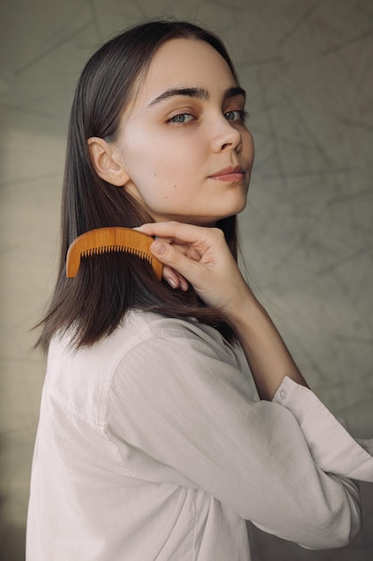 retrato de mulher escovando cabelos castanhos com pente de madeira ao fazer rotina diária de beleza