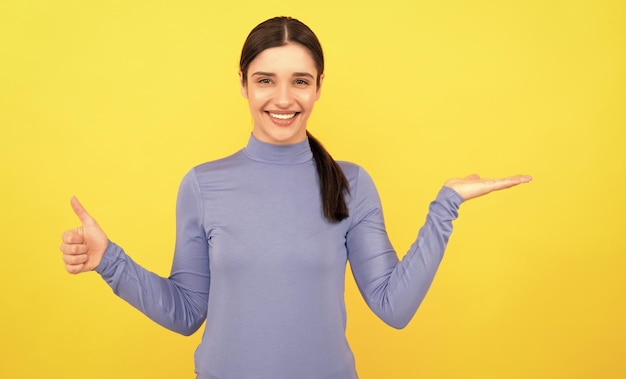 Retrato de mulher espantada apontando dedos no espaço de cópia fundo amarelo mostrando o polegar para cima emoções