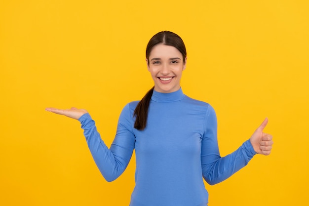 Retrato de mulher espantada apontando dedos no fundo amarelo do espaço de cópia mostrando o polegar para cima, emoções