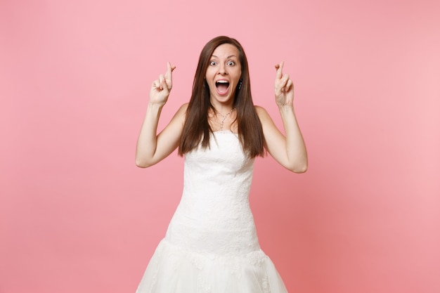 Foto retrato de mulher excitada em vestido branco espera por momento especial, mantendo os dedos cruzados, fazendo desejo