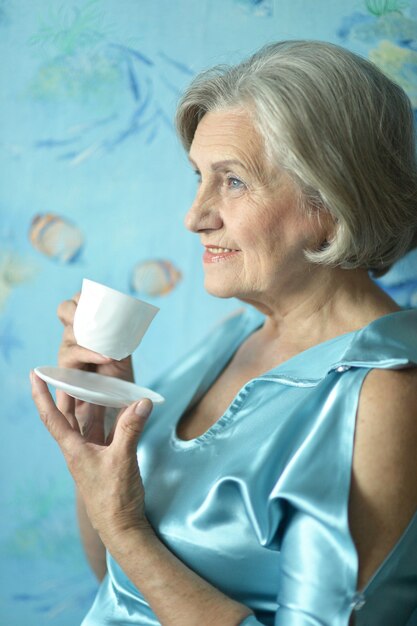 Retrato de mulher feliz aposentada bebendo chá sobre fundo azul