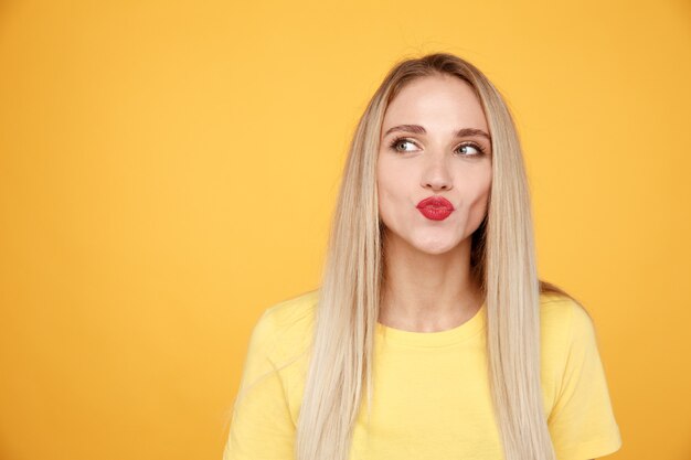 Retrato de mulher feliz beijando seus lábios vermelhos no estúdio amarelo