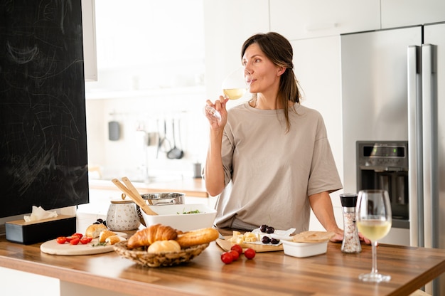 Retrato de mulher feliz com legumes e copo de vinho na cozinha em casa