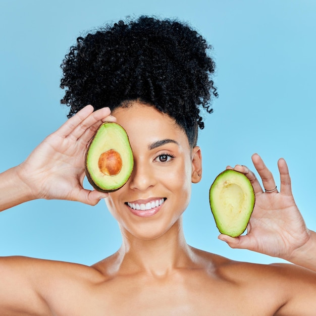 Foto retrato de mulher feliz e abacate para dieta de cuidados com a pele ou beleza natural contra um fundo de estúdio azul rosto de pessoa feminina sorri com frutas orgânicas para nutrição vitamina c ou bem-estar da pele