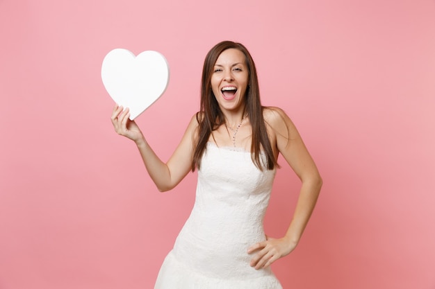 Retrato de mulher feliz e animada em um elegante vestido branco em pé segurando um coração branco com espaço de cópia