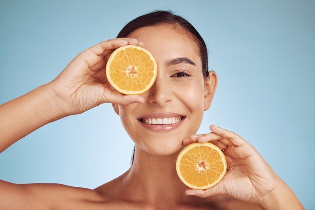 Foto retrato de mulher feliz e laranja para cuidados com a pele natural de vitamina c ou dieta contra um fundo de estúdio azul rosto de sorriso de pessoa com frutas cítricas orgânicas em dermatologia nutricional ou bem-estar saudável