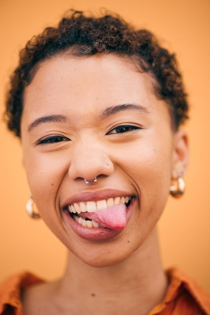 Retrato de mulher feliz e língua de fora em estúdio com sorriso e sensação de confiança boba Fundo laranja jovem e mulher africana com moda moderna e estudantil com piercing gen z