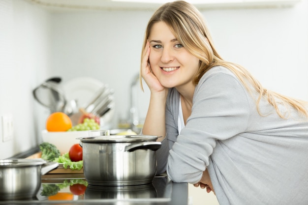 Retrato de mulher feliz e sorridente, posando na cozinha e cozinhando sopa