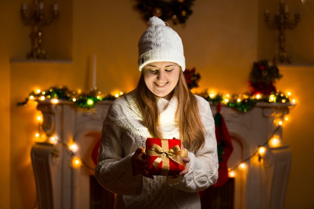 Retrato de mulher feliz em suéter segurando uma caixa de presente brilhante na véspera de Natal
