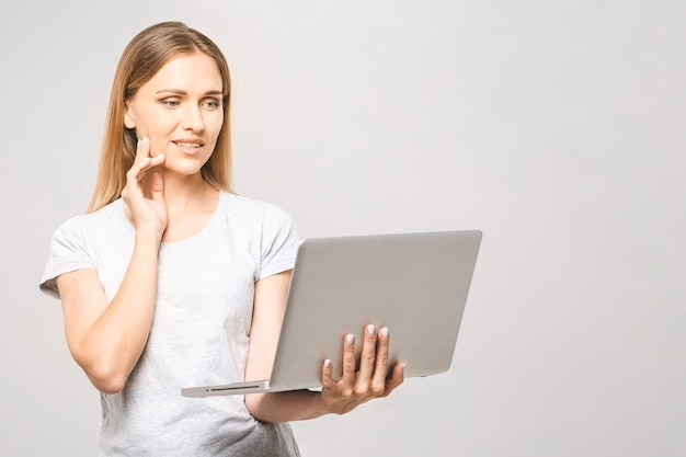 Retrato de mulher feliz jovem bonita pensando em pé com laptop isolado no fundo branco. Espaço para texto.