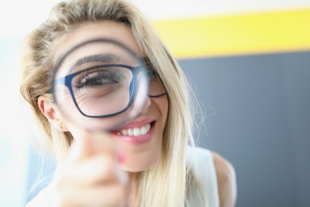 Retrato de mulher feliz, se divertindo e olhando através da lupa. Loira atraente usando óculos pretos da moda e curtindo. Pessoa entusiasmada. Conceito de alegria e felicidade