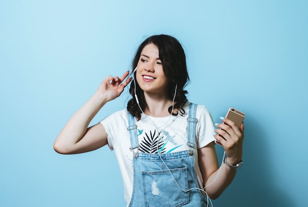 Retrato de mulher feliz usando fones de ouvido cantando isolado sobre parede azul