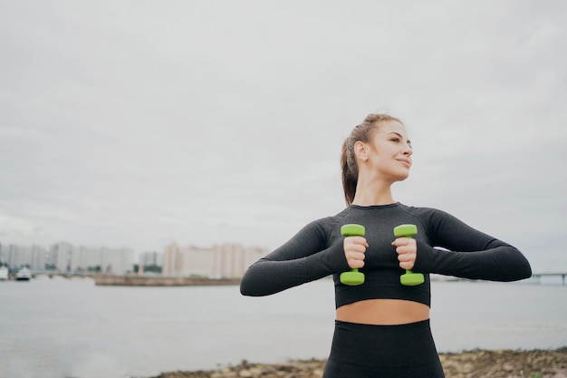 Retrato de mulher fitness de uma morena determinada faz exercícios para braços com halteres