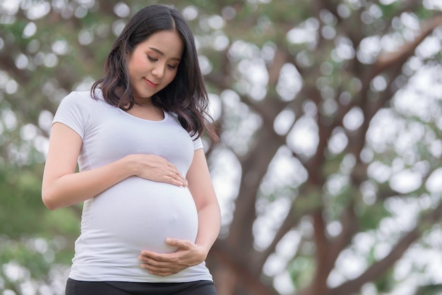 Foto retrato de mulher grávida bonita asiática no parquepovo da tailândiaconceito de mulher felizsua mão de uso toca sua barrigaconceito de dia das mães