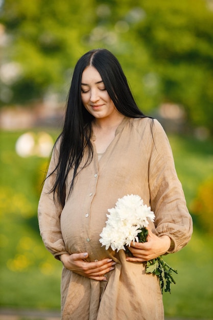 Retrato de mulher grávida de vestido bege em pé em um parque