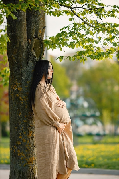 Retrato de mulher grávida de vestido bege em pé em um parque