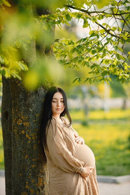 Retrato de mulher grávida de vestido bege em pé em um parque