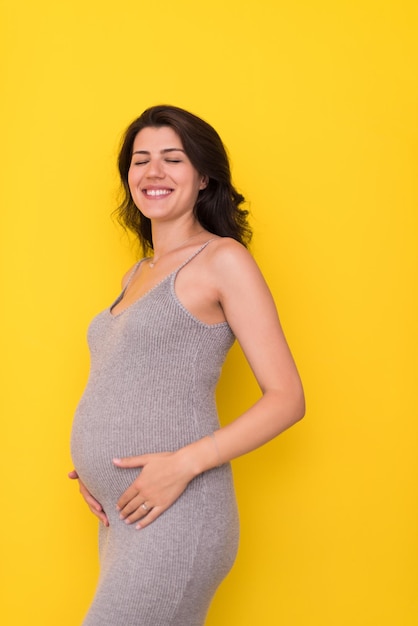 Retrato de mulher grávida feliz com as mãos na barriga isolada sobre fundo amarelo