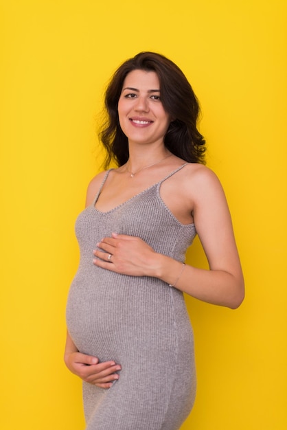 Retrato de mulher grávida feliz com as mãos na barriga isolada sobre fundo amarelo