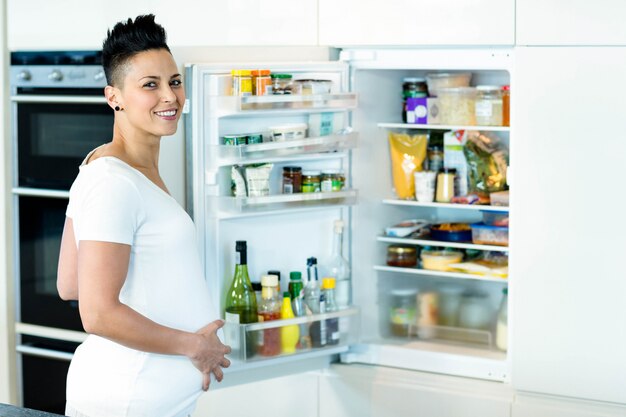 Retrato de mulher grávida sorrindo enquanto procurava comida na geladeira