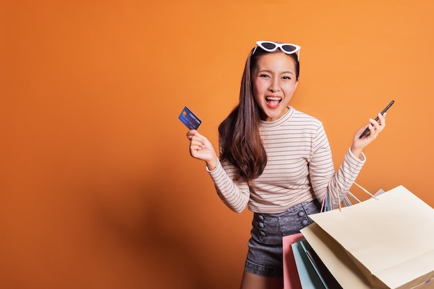 Foto retrato de mulher gritando com sacos de compras e cartão enquanto está de pé contra um fundo laranja