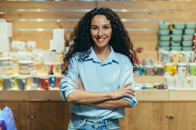 Retrato de mulher hispânica proprietária de negócios gerenciando mulher de loja de presentes com cabelo encaracolado olhando para a câmera