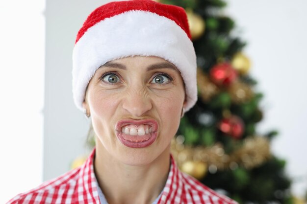 Retrato de mulher irritada com chapéu de papai noel no fundo das emoções da árvore de natal