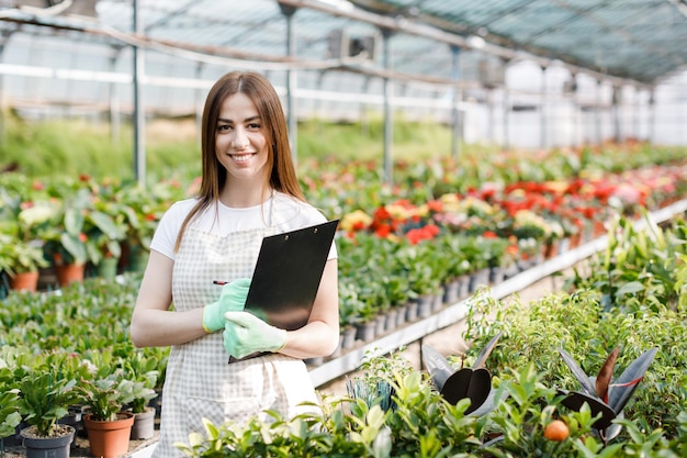 Retrato de mulher jardineira no trabalho em estufa com notebook examina as flores em crescimento na estufa Jardinagem doméstica amor de plantas e cuidados Pequenas empresas