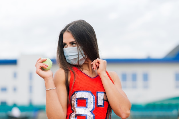 Foto retrato de mulher jogadora de tênis segurando uma bola do lado de fora com máscaras protetoras