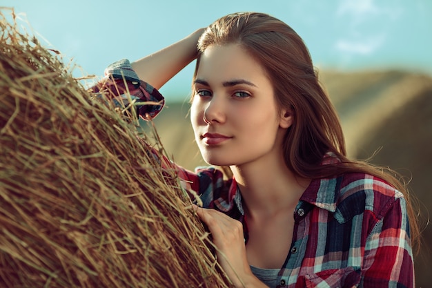 Retrato de mulher jovem ao lado de uma pilha de feno sob a luz do sol