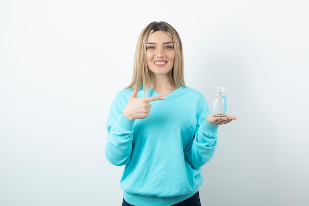 Retrato de mulher jovem apontando para um jarro de vidro com água na mão