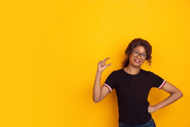 Retrato de mulher jovem bonita afro-americana em fundo amarelo do estúdio, emocional