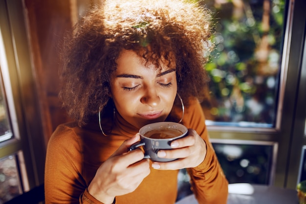 Retrato de mulher jovem bonita de raça mista com cabelos cacheados, sentado no refeitório e desfrutar de café.