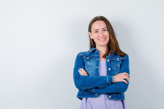 Retrato de mulher jovem com os braços cruzados na jaqueta jeans e olhando alegre para a frente