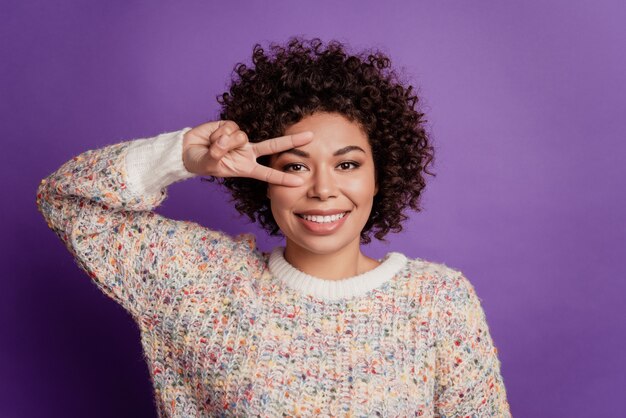 Retrato de mulher jovem e alegre mostrando o olho da capa do símbolo V isolado no fundo roxo