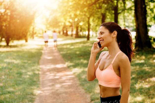 Retrato de mulher jovem e bonita atleta falando no telefone no parque da cidade