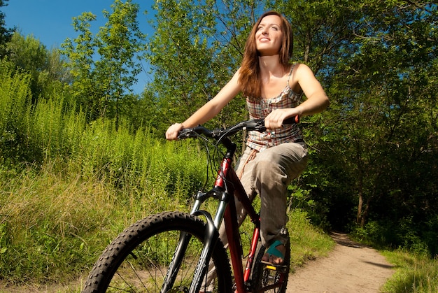 Retrato de mulher jovem e bonita com bicicleta em um parque sorrindo - ao ar livre