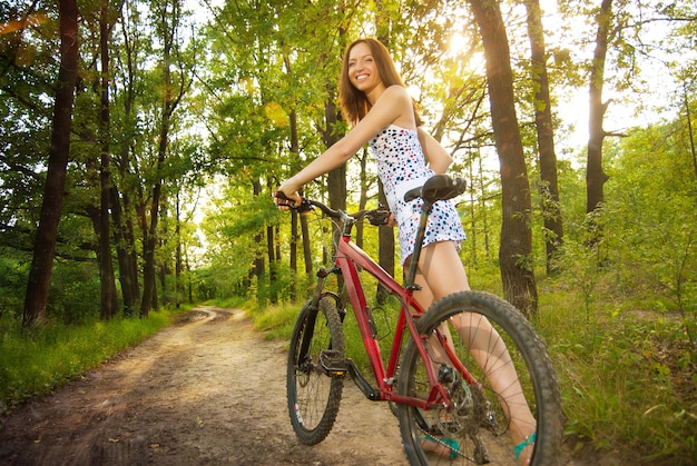 Retrato de mulher jovem e bonita com bicicleta em um parque sorrindo - ao ar livre